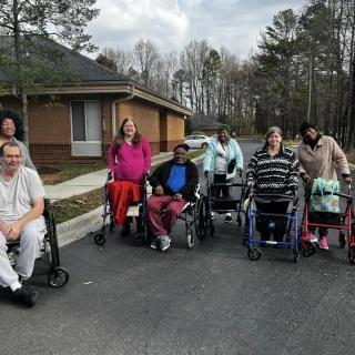 A group of people in wheelchairs gathered outdoors near a building.