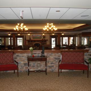 A warmly lit lobby area with symmetrical seating, chandeliers, and a central fireplace flanked by mirrors.
