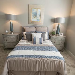 A cozy bedroom with a neatly made bed, flanked by bedside tables and lamps, featuring soft and calming colors.