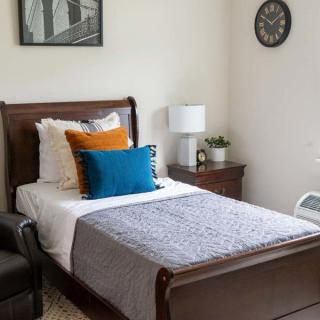 A cozy bedroom with a single wooden bed, colorful pillows, and a neatly arranged nightstand.