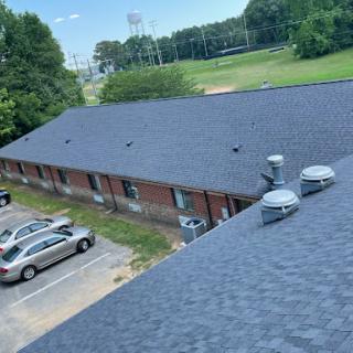 Aerial view of a building's roof with parked cars and a green field in the background.