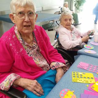 Two elderly women playing bingo together at an indoor setting.