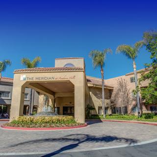 The exterior of a hospital entrance with palm trees and clear blue skies.