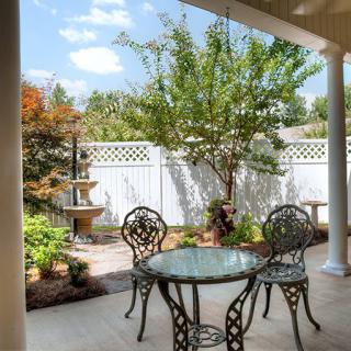 A serene patio with elegant wrought iron furniture surrounded by a lush garden and decorative fountain.