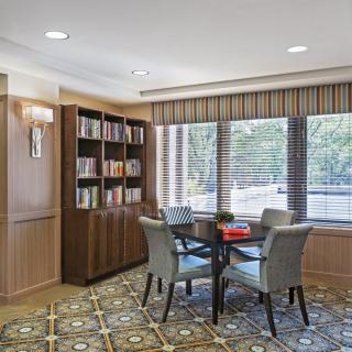 A cozy reading area with a table and chairs surrounded by bookshelves and natural light from the window.