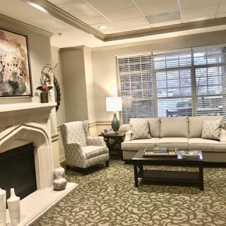 A cozy and elegantly decorated living room with a fireplace, sofa, armchair, and large window.