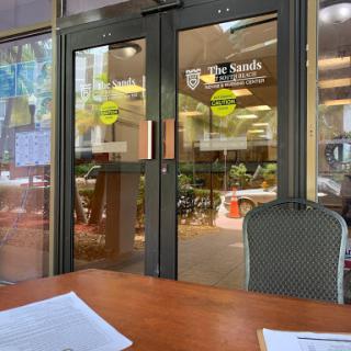 A view of the entrance to a restaurant, featuring glass doors and outdoor seating.