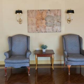 A cozy sitting area featuring two armchairs and a small wooden table with a potted plant, accented by wall sconces and artwork above.