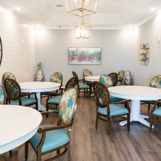 A well-decorated dining room featuring round tables, cushioned chairs, elegant light fixtures, and wood flooring.