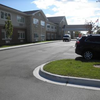 A view of a hotel with a parking lot and landscaped area under a partly cloudy sky.