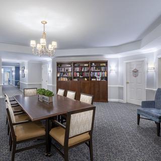 A well-lit conference room with a central meeting table, chairs, and a bookshelf in the background.