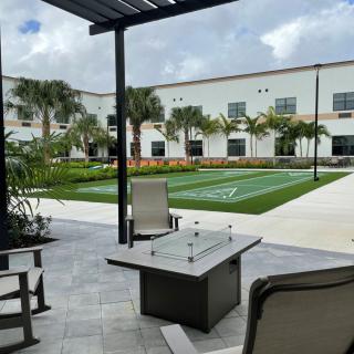 A modern patio area with a fire pit table and outdoor seating overlooking a landscaped lawn with palm trees.