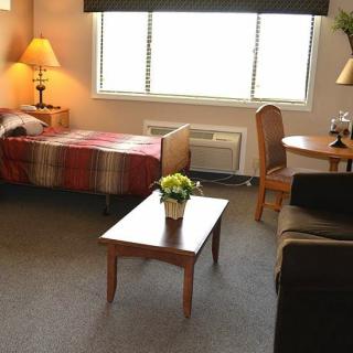 A cozy hotel room with a bed, table, chair, and lamp.