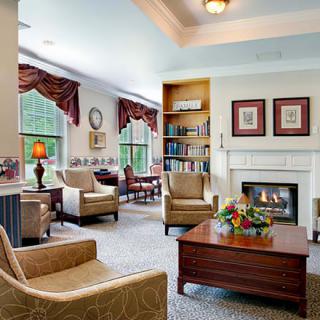 A cozy living room with comfortable armchairs, a central fireplace, and large windows letting in natural light.