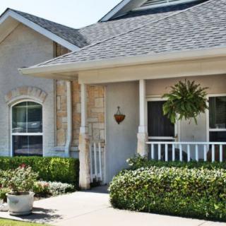 A cozy house with a welcoming front porch, featuring well-maintained landscaping and decorative plants.