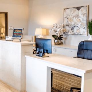 A modern reception desk with a computer, chair, artwork, and decorative plants.