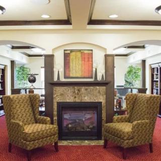 A cozy living room featuring two patterned armchairs facing a fireplace, with artwork and plants enhancing the decor.