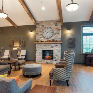 A cozy living room with a stone fireplace, large clock, and comfortable armchairs.