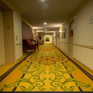 A brightly lit hotel hallway with patterned carpet and seating.