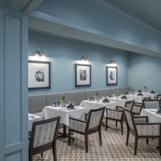 A tastefully designed restaurant dining area with blue walls, neatly arranged tables and chairs, and framed artwork.