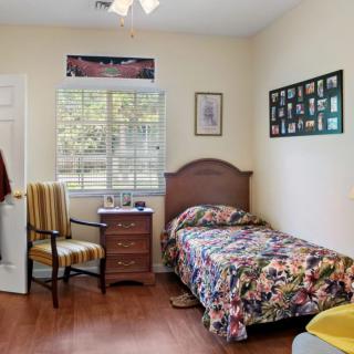 A cozy bedroom with a single bed, floral bedding, a nightstand with decor, and a chair by the window.