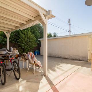 A sunny backyard patio area with bicycles, chairs, and a pergola.