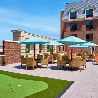 A rooftop patio with wicker furniture and umbrellas under a clear blue sky, adjacent to a brick building.