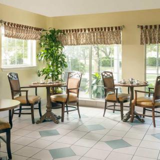 A cozy dining area with tables and chairs, featuring large windows and an indoor plant.