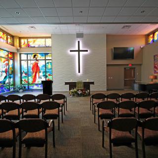 A serene church interior featuring a prominent cross and vibrant stained glass windows.