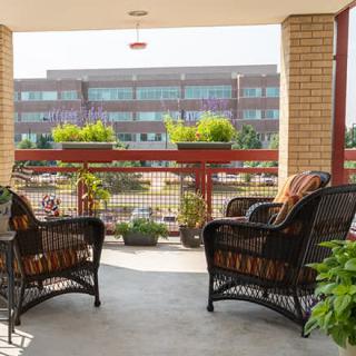 A cozy balcony with wicker chairs and potted plants overlooking a modern building.