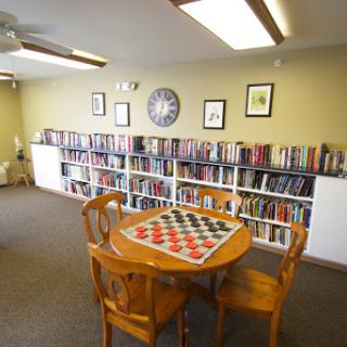 A cozy library space featuring bookshelves filled with books, a wooden table with a board game, and comfortable seating.