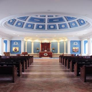 A grand hall with symmetrical wooden seating and a blue domed ceiling.