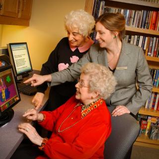 Three women engaging with a computer in a library setting.
