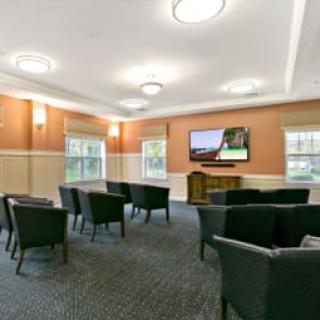 A meeting room with chairs facing a television and windows letting in natural light.