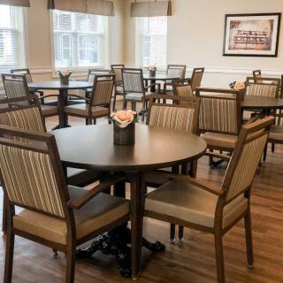 A dining area with neatly arranged tables and chairs, featuring wood flooring and a framed picture on the wall.