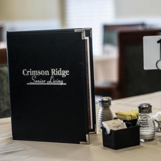A restaurant table setup with a menu from Crimson Ridge Senior Living and various condiments.