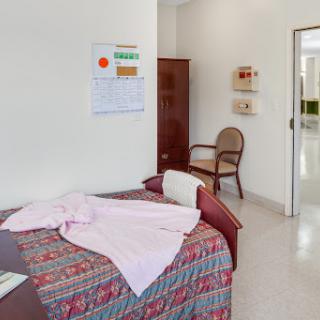 A tidy bedroom featuring a bed with colorful bedding, a chair, and a wall calendar.