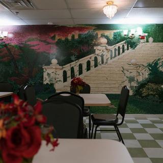 A cozy restaurant interior with a mural depicting a scenic staircase and lush greenery.