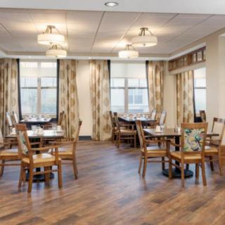 A well-lit dining area with wooden flooring and elegantly arranged tables and chairs.