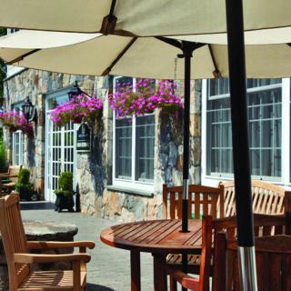 A cozy outdoor patio with wooden furniture and large umbrellas, adorned with hanging flowers.