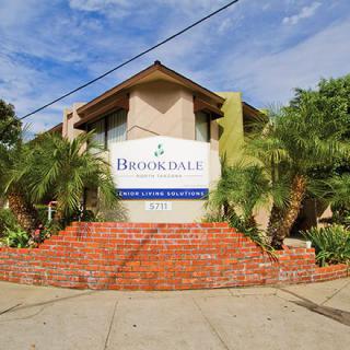 The image features the Brookdale Senior Living building, surrounded by palm trees and a brick entrance.