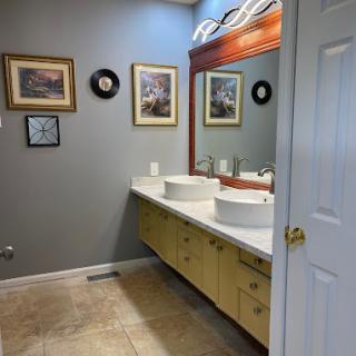 A modern bathroom with dual sinks, large mirror, and decorative artwork on the walls.