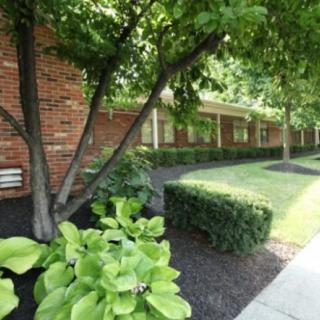 A serene view of a brick building with surrounding lush greenery and a sidewalk.
