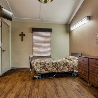 A small room with a hospital bed, cross on the wall, and wooden flooring.