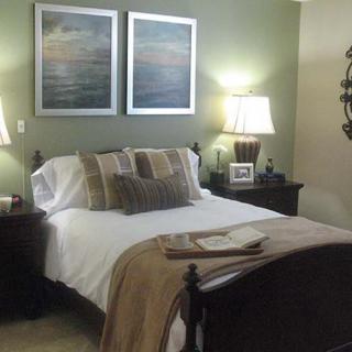 A cozy bedroom with a neatly made bed, soft lighting from table lamps, and artwork on the walls.