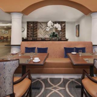 A cozy restaurant interior featuring banquette seating with decorative pillows and elegant table settings, complemented by a centerpiece of orchid flowers.
