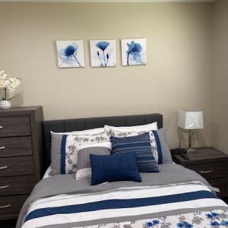 A neatly arranged bedroom with blue and grey decor, featuring wall art and coordinating bedding.