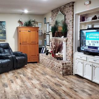 A cozy living room with a leather couch, wooden floors, a brick fireplace, and a TV setup.