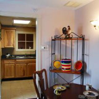 A cozy kitchen and dining space with wooden cabinets and a decorative shelf displaying colorful dishes.