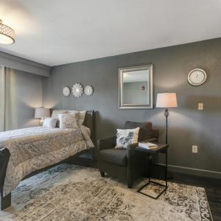 A modern bedroom with grey walls, featuring a cozy bed, an armchair, and stylish lighting.